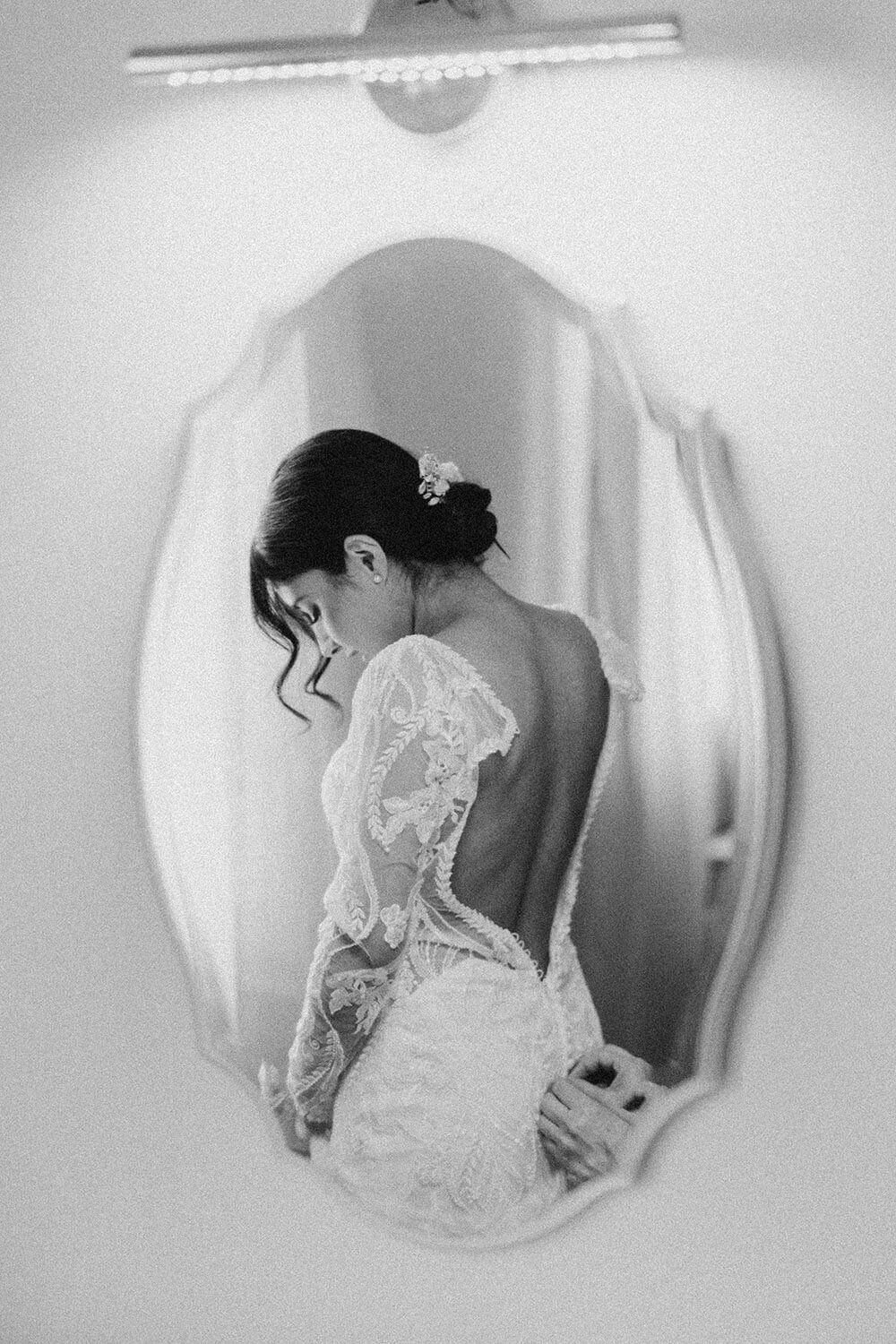 Bride in lace wedding gown admiring her reflection in a mirror before the wedding.