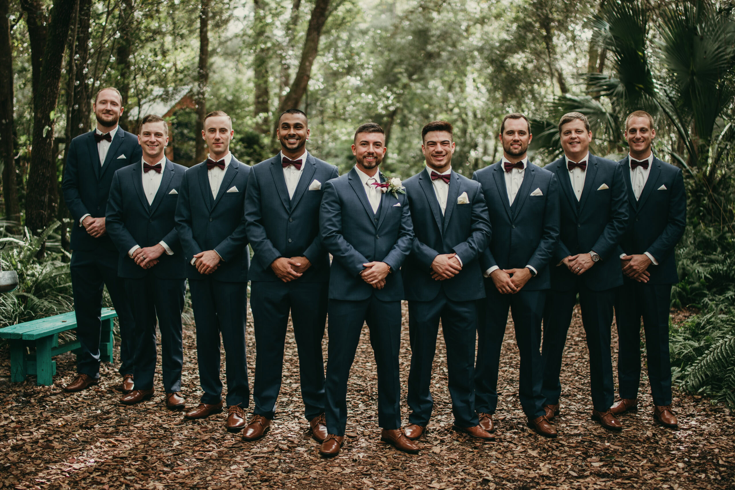 Groomsmen in navy suits at wedding, standing in a natural forest environment.