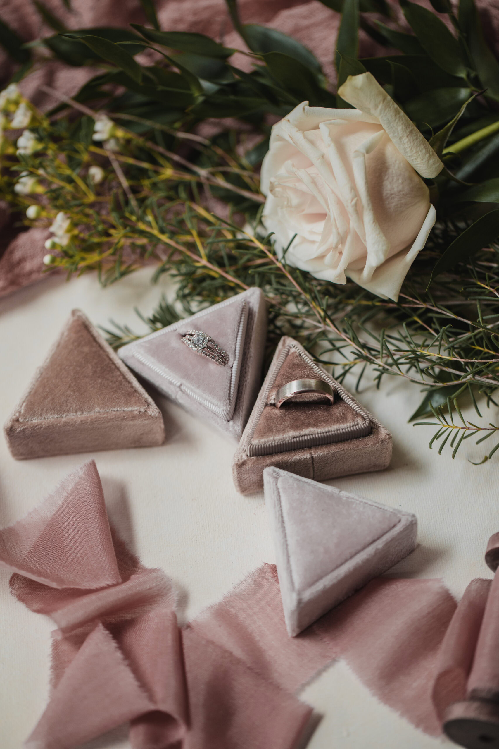Elegant wedding rings and jewelry displayed with a white rose and greenery.