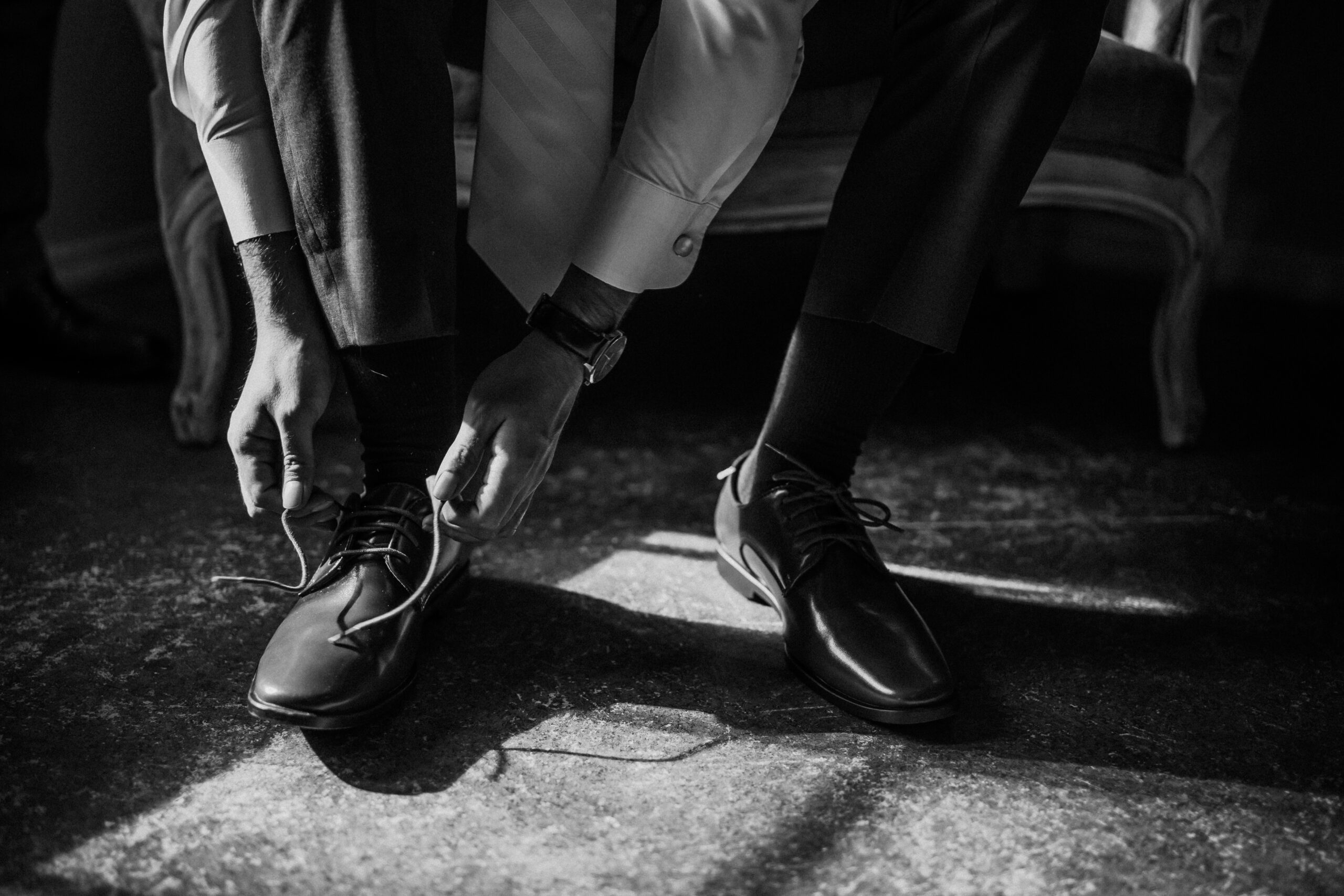 Groom tying his shoelace while sitting on a vintage sofa, preparing for his wedding day.